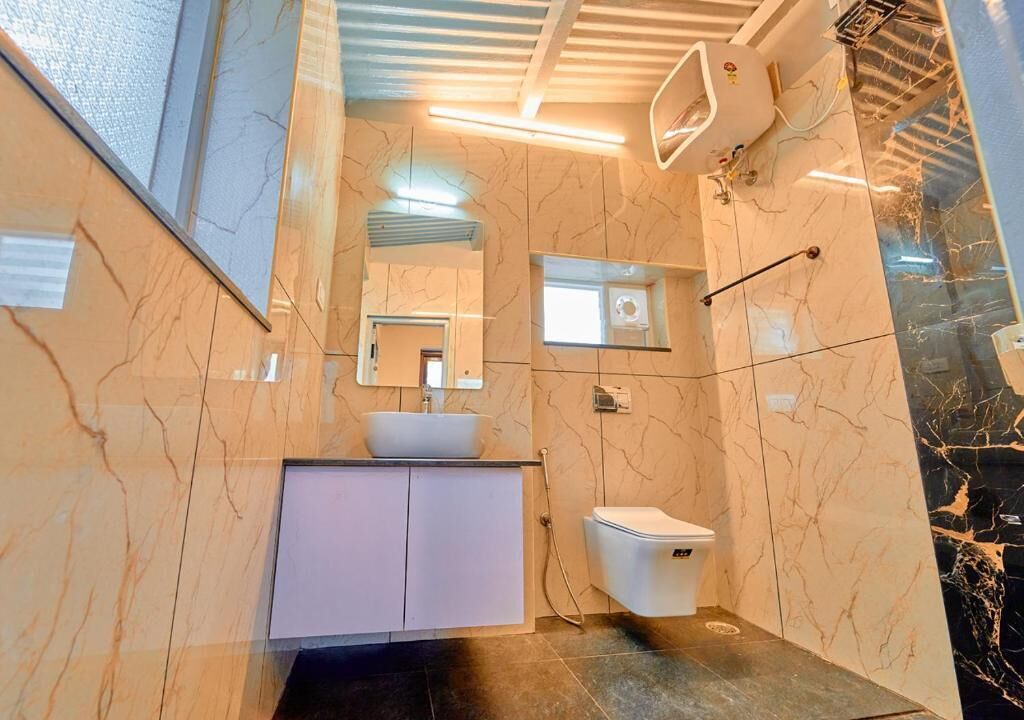 A bathroom with a marble wall, a white sink, a mirror, and a toilet.