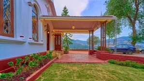Un edificio con entrada cubierta, un jardín con plantas y vistas a las montañas.