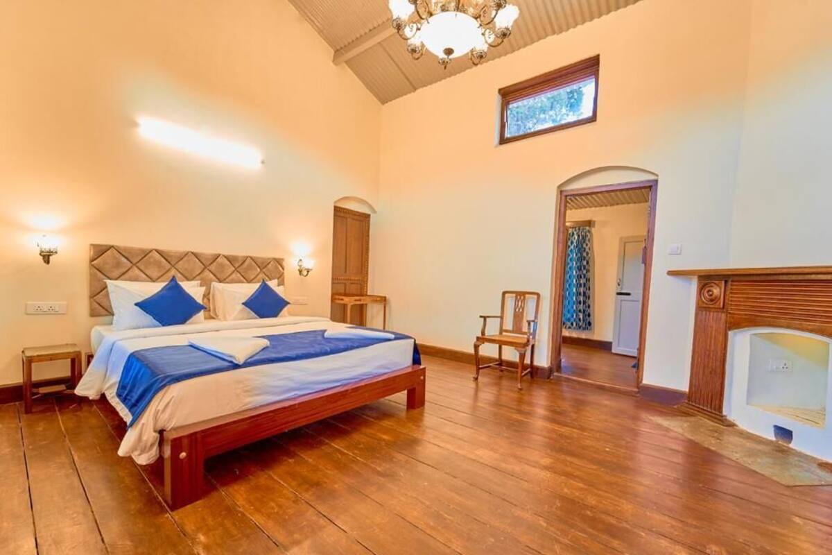 A bedroom with a wooden bed, two bedside tables, a chair, a fireplace, and a chandelier.