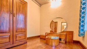 Un armario de madera, un espejo redondo y un taburete pequeño en una habitación con suelo de madera.