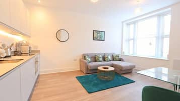 A modern apartment with a kitchen, a sofa, a dining table, and a large window.