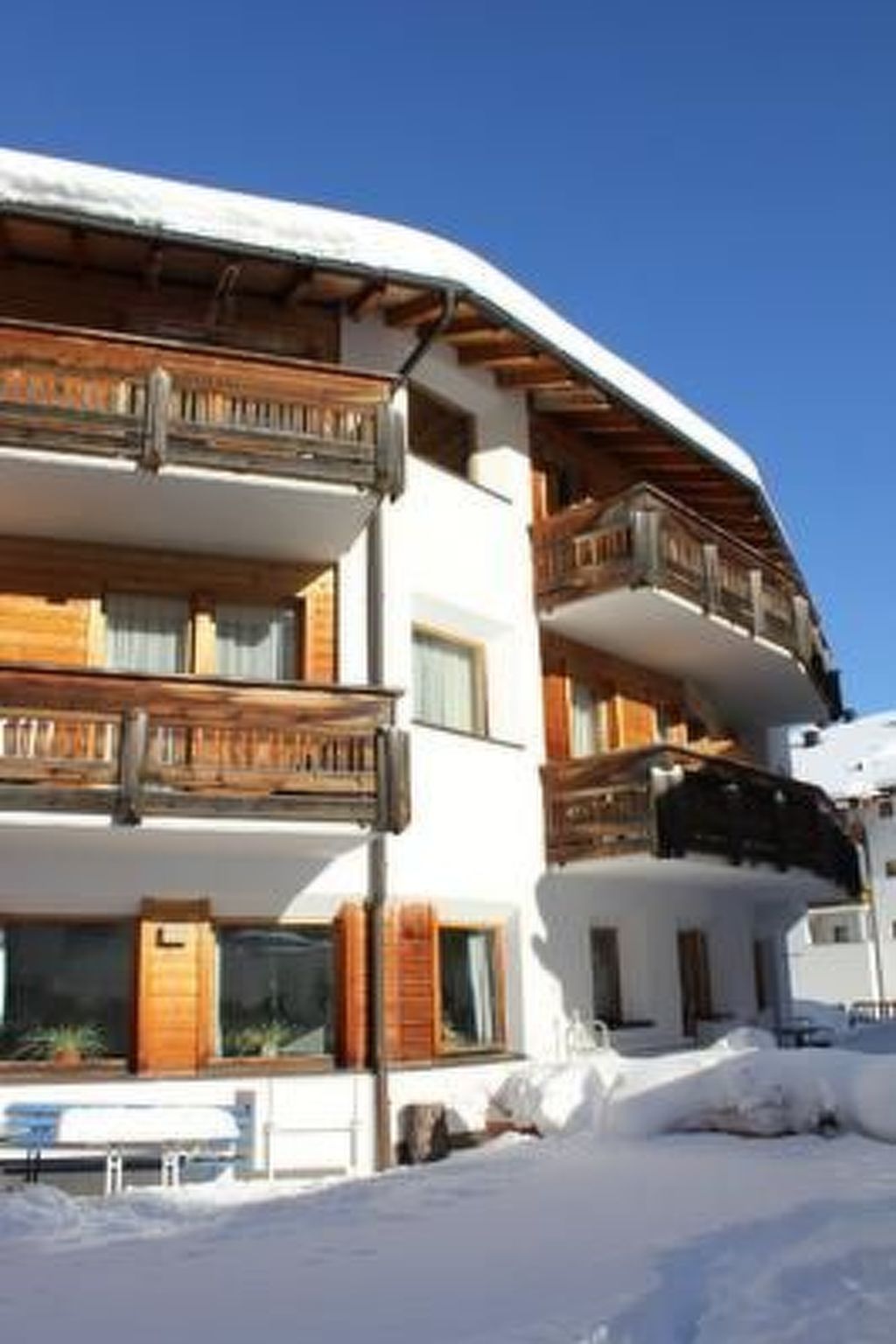 A multi-story building with balconies, wooden railings, and a snow-covered ground.