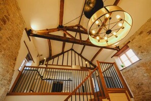 A rustic interior with exposed wooden beams, a staircase with a metal railing, and a hanging light fixture. - The Granary- Hopewell (Bristol)