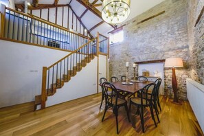 A dining area with a wooden table and chairs, a staircase with wooden railings, and a stone wall. - The Granary- Hopewell (Bristol)