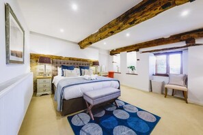 A bedroom with a bed, bedside tables, a bench, a window, and a wooden ceiling beam. - The Granary- Hopewell (Bristol)