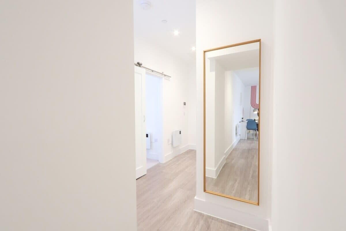 A hallway with a large mirror, a door, and a glimpse of a bathroom with a blue chair.