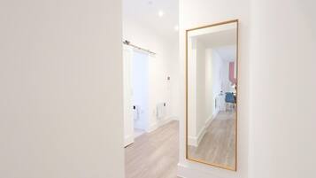 A hallway with a large mirror, a door, and a glimpse of a bathroom with a blue chair.