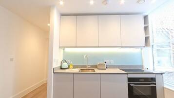 A compact kitchen with a sink, toaster, kettle, and oven.