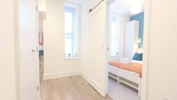 A bedroom with a bed, a window, and a door leading to another room.