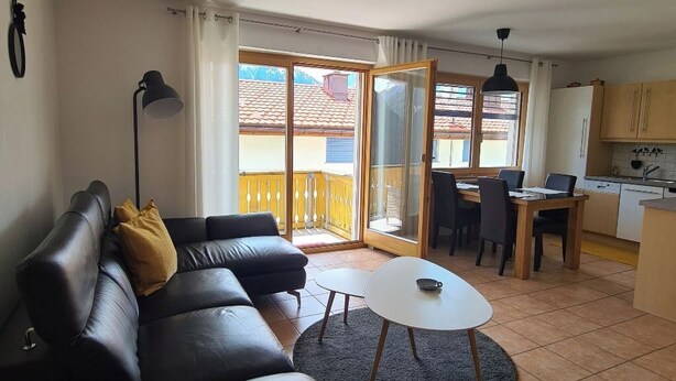 A living room with a black leather sofa, a round coffee table, and a dining area with a table and chairs. - Scandella, (Sent) by Interhome (Sent)