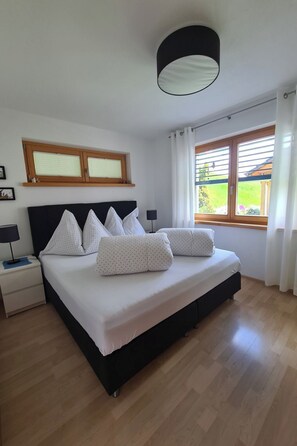 A bedroom with a bed, a nightstand, a lamp, a window with curtains, and a ceiling light fixture. - Scandella, (Sent) by Interhome (Sent)