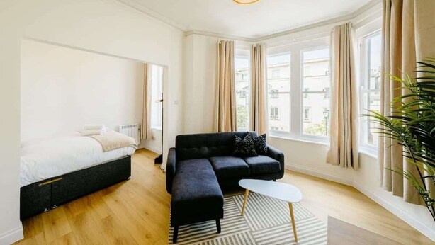 Una habitación moderna con cama, sofá, una mesita y un amplio ventanal con cortinas.