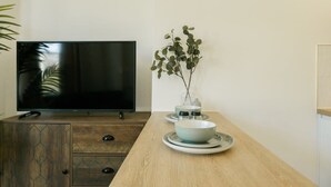 Una sala de estar moderna con televisor de pantalla plana, un mueble de madera y una mesa de comedor con un jarrón con plantas.