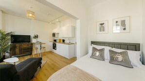 Una habitación de hotel moderna con cama, televisor, kitchenette y mesa de comedor.