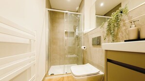 Un baño moderno con ducha envuelta en vidrio, inodoro blanco y suelo de madera.