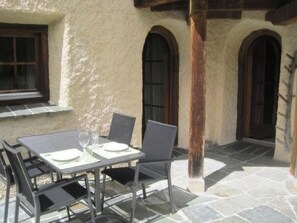 An outdoor patio with a table set for two, surrounded by stone flooring and wooden arches.