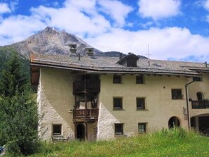 Un chalet de montagne à la façade en pierre, doté de nombreuses fenêtres et d’un balcon.
