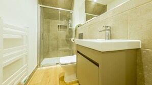 Moderni kylpyhuone, jossa on lasinen suihkuseinä, valkoinen pesuallas ja wc-istuin.