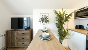 Moderni keittiö, jossa on puinen pöytä, litteänäyttöinen televisio, mikroaaltouuni ja ruukkukasvi.