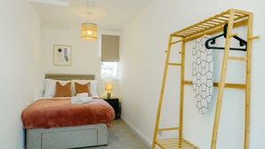 Quarto com cama, mesa de cabeceira, abajur e uma estrutura de escada de madeira na parede.