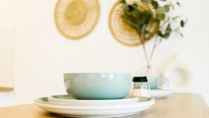 Een tafel met een kom en schotel, een vaas met groen, en een muur met ronde decoraties.