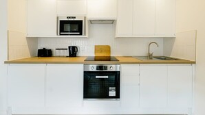 Een kleine keuken met witte kastjes, een magnetron, een koffiezetapparaat, een spoelbak en een oven.