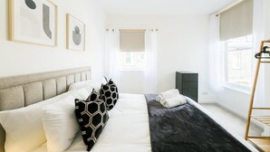 Een moderne slaapkamer met een bed, kussens, een nachtkastje, een kledingkast en een raam met gordijnen.