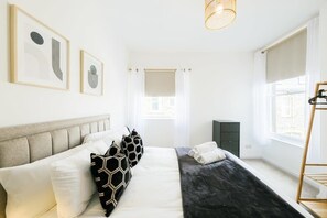Ein modernes Schlafzimmer mit Bett, Kissen, Nachttisch, Kleiderschrank und einem Fenster mit Vorhängen.