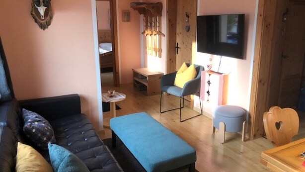 Un salon chaleureux avec un canapé, une petite table, un banc bleu, une table à manger en bois et un téléviseur.