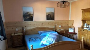 Un lit en bois avec une couvre-lit bleue, deux tableaux accrochés au mur, une lampe de chevet, une table de chevet en bois et une armoire en bois.