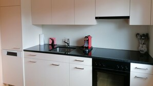 Une cuisine avec des meubles blancs, un plan de travail noir, un évier, un appareil électroménager rouge et une cuisinière.