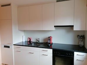 A kitchen with white cabinets, a black countertop, a sink, a red appliance, and a stove.