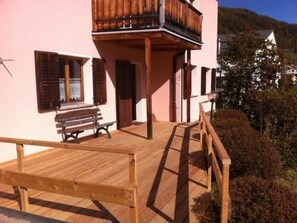 Une terrasse en bois avec un banc, un balcon et une vue sur une colline boisée.