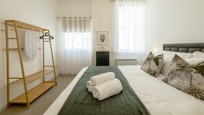 Un dormitorio con una cama, un tendedero de madera, una manta verde y una almohada con motivos tropicales.