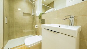 Un baño con ducha de vidrio, inodoro blanco y lavamanos con grifo cromado.