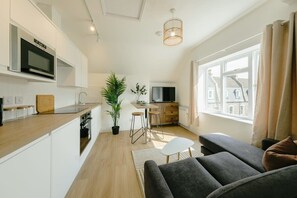 A modern kitchen with a microwave, a dining area with stools, a sofa, and a television. - Grange Rd Flat 5 one bedroom (Bristol)