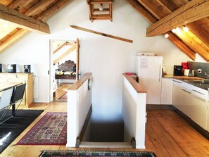 Een kleine keuken met een houten plafond, een koelkast, een wastafel en een eethoek met stoelen.