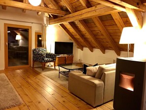 A cozy living room with a wooden ceiling, a sofa, a patterned armchair, a glass coffee table, and a television. - Chasa d'Uina, (Sent) by Interhome (Sent)