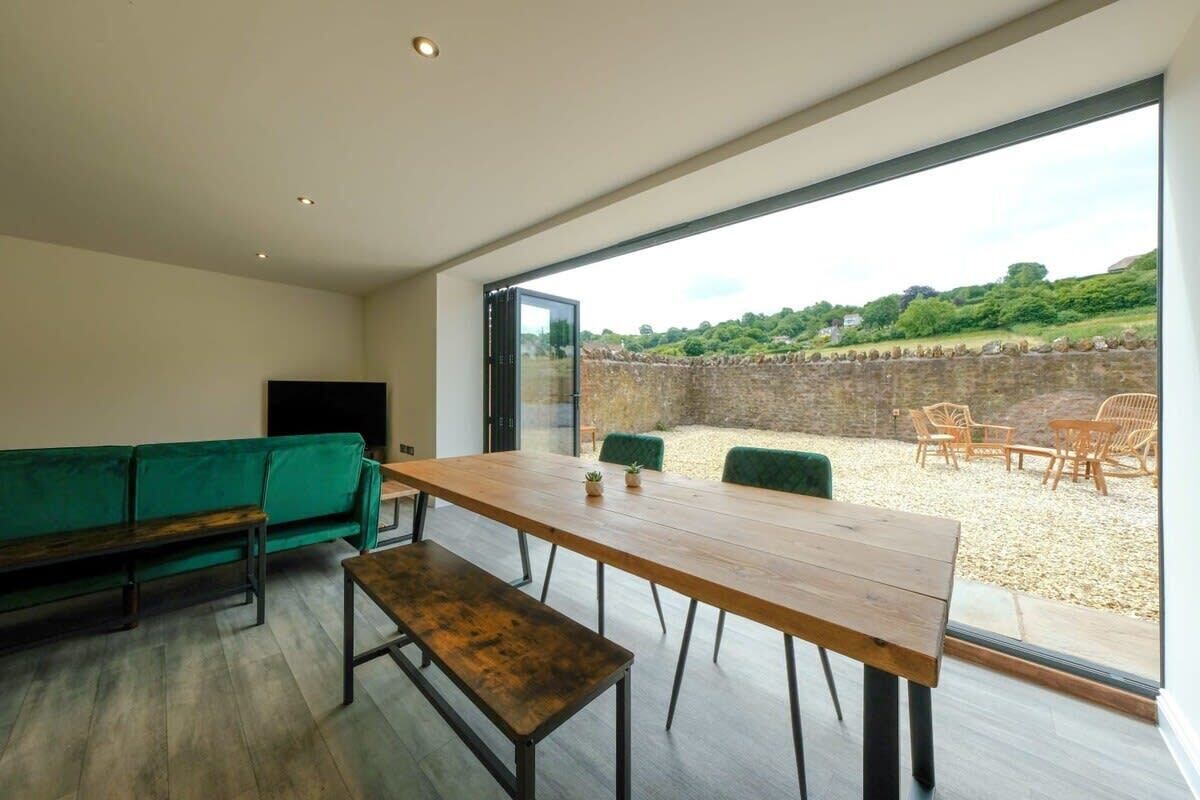 Een modern interieur met een houten eettafel, een groene bank en uitzicht op een terras.
