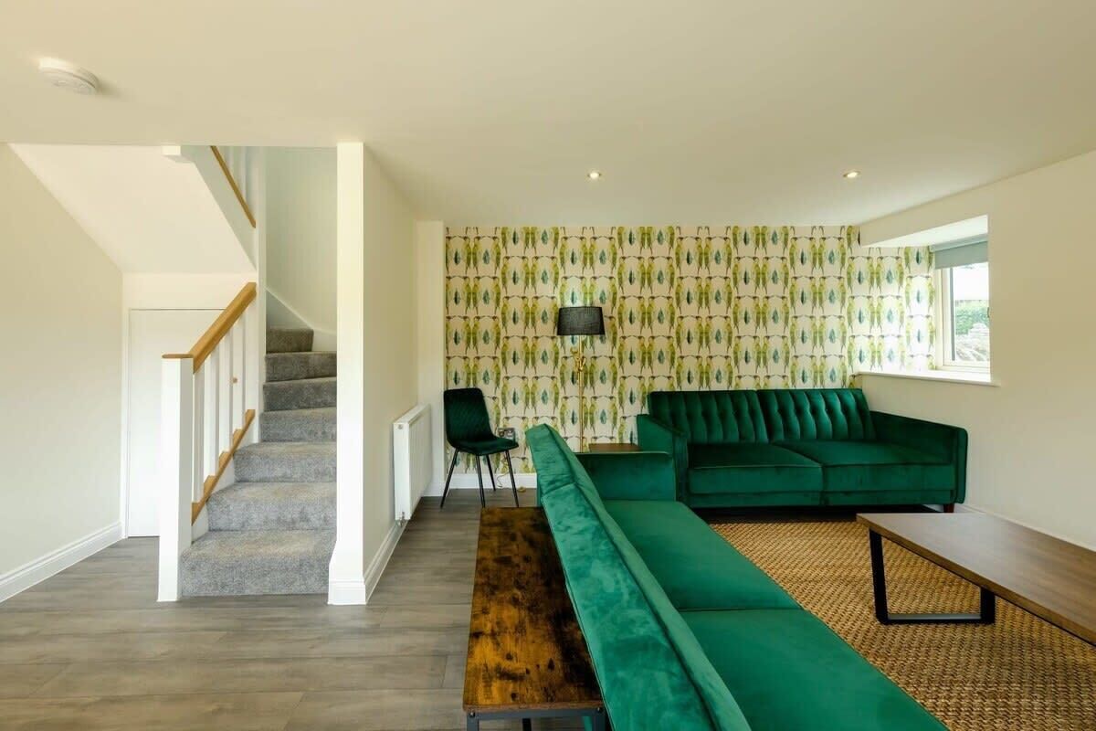 A modern living room with a staircase, green sofa, and patterned wallpaper.