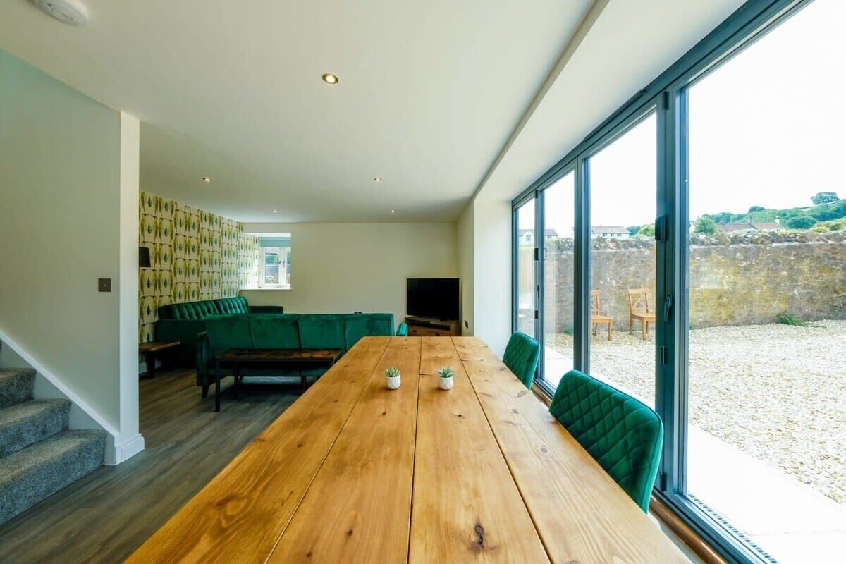 Una sala moderna con una mesa de comedor de madera, un sofá tapizado en tonos verdes y un televisor.
