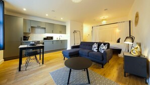 A modern living room with a sofa, a dining table, and a kitchen in the background. - Hotwells apartments flat 1 - Hopewell (Bristol)