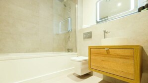 A modern bathroom with a bathtub, a toilet, a wooden vanity with a mirror, and a shower area. - Hotwells apartments flat 2 - Hopewell (Bristol)