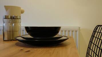 Une table en bois sur laquelle se trouvent un bol et une assiette noirs, un pichet de couleur crème et deux récipients métalliques.