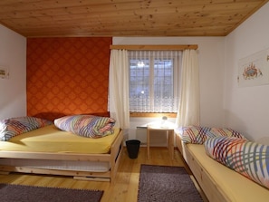Una habitación con dos camas, una ventana con cortinas, una mesita pequeña y un cubo de basura.