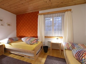 Ein kleiner, gemütlicher Raum mit zwei Betten, einem Schreibtisch und einem Fenster mit Vorhängen.