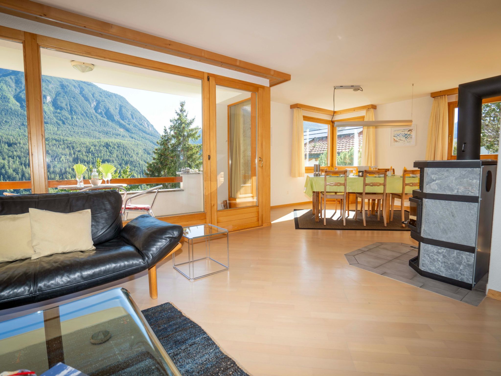 A modern living room with a leather sofa, a dining area with wooden chairs, and a kitchen with a stove.