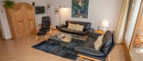 A living room with a sofa, armchairs, a coffee table, a TV, and artwork on the wall.