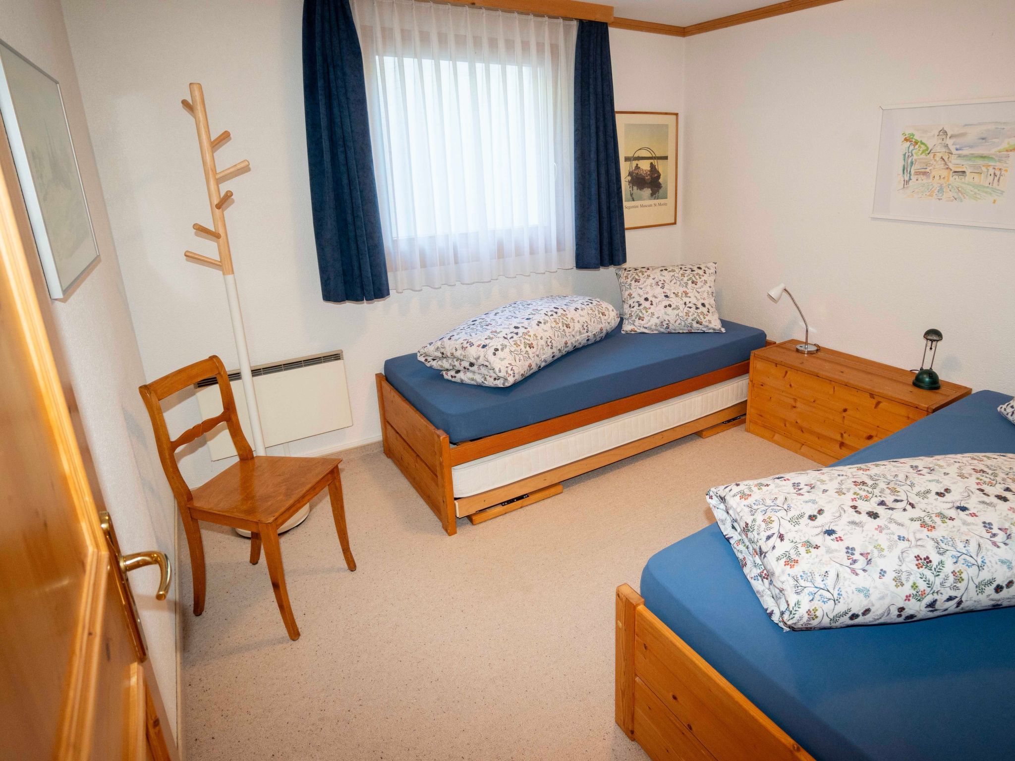 A bedroom with a bed, a chair, a desk, and a window with curtains.