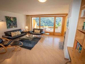 Uma sala de estar moderna com um sofá de couro preto, uma mesa de centro de vidro e uma estante de madeira.